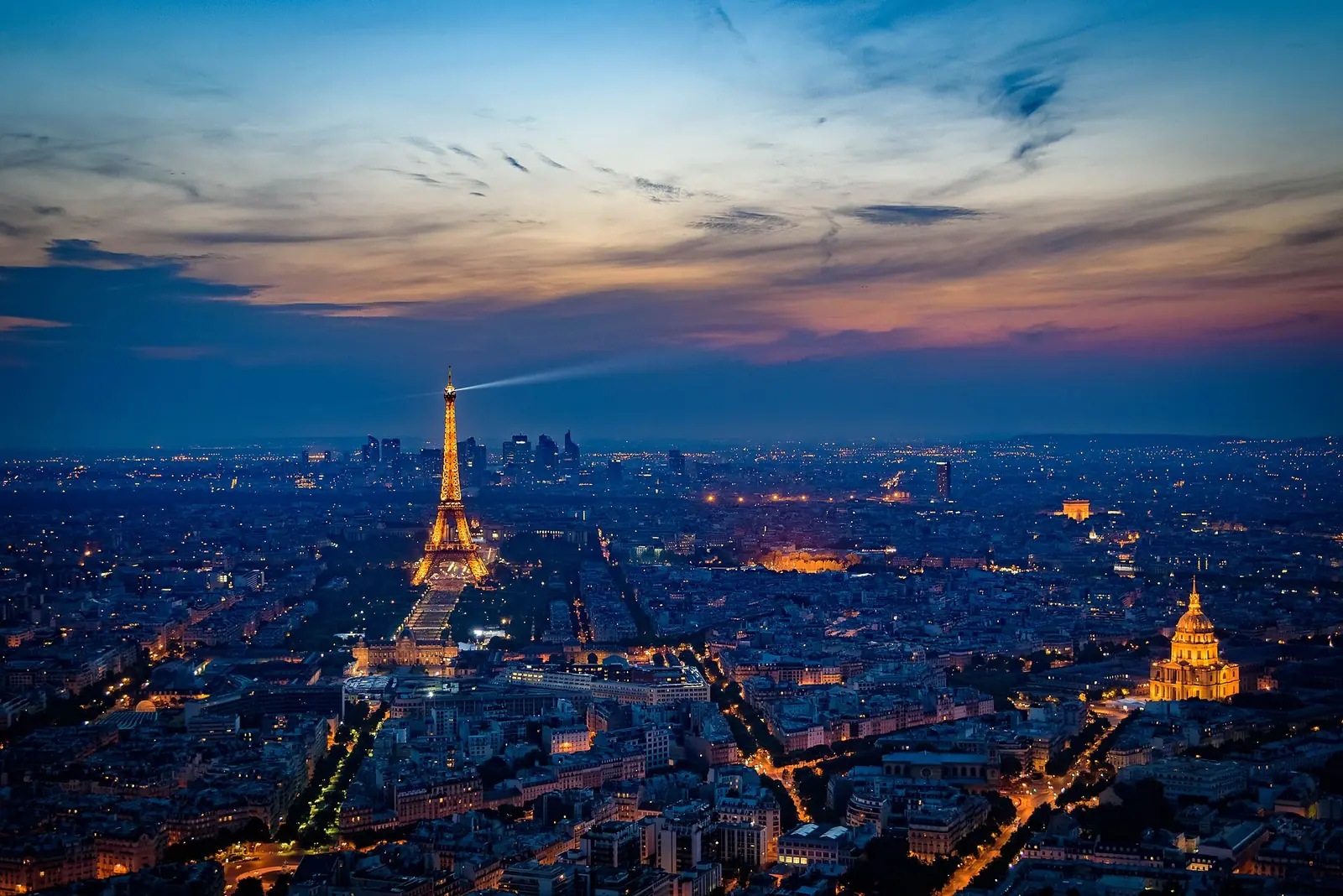 The Eiffel Tower lit at dusk above the rooftops of Paris